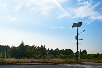 A solar-powered streetlight standing tall by a pedestrian crossing in a quiet, rural area.
