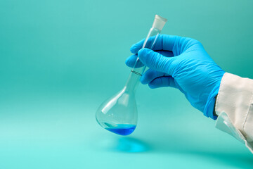 hand with volumetric flask that has a blue chemical liquid.