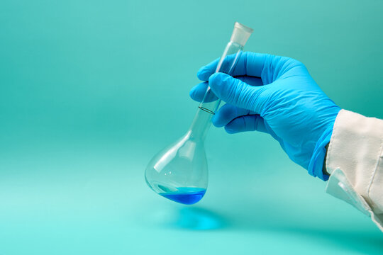 hand with volumetric flask that has a blue chemical liquid.