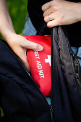 A person is carefully placing a first aid kit into their backpack, ensuring that it fits snugly and securely inside, as they prepare for their next adventure or activity