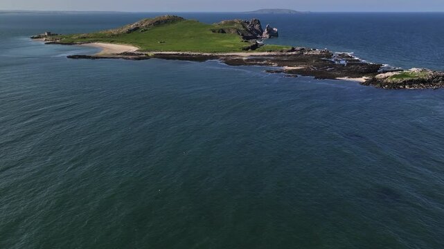 Ireland's Eye, County Dublin, Ireland, May 2023. Drone tilts up to reveal the picturesque Isle's beach and rugged landscape on a bright sunny day with Lambay Island on the horizon.