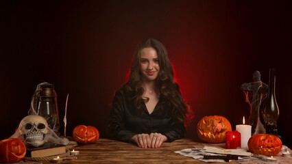 Halloween gothic woman witch fortune teller sitting at table playful face expression, happy smiling. Magic halloween concept.