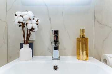 In a stylish bathroom, there is a lovely sink alongside a vibrant vase filled with beautiful cotton...
