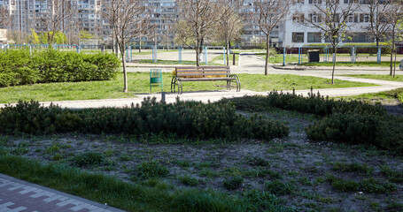 Obraz premium Rest area with bench surrounded by trees and ornamental shrubs in Kyiv, Europe. Place to rest in the city park at spring