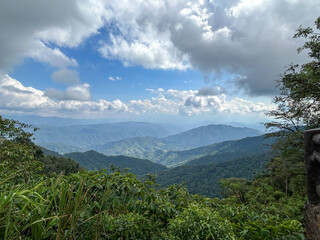 Mountain view against the sky. Aerial top view above green pass to rocky deep gorge with sharp sheer crags silhouettes against huge mountain under clouds in blue sky. 