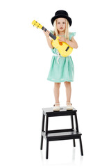Fashion, guitar and portrait of child in studio on step for playing music, practice and learning songs. Childhood, creative and isolated young girl with musical instrument toy on white background