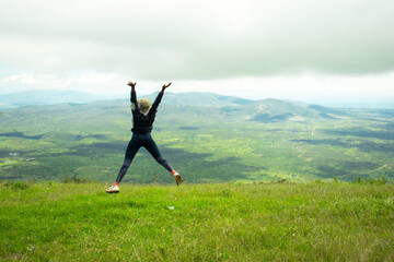 A young black woman frolicking in the grass in the hills after a hike