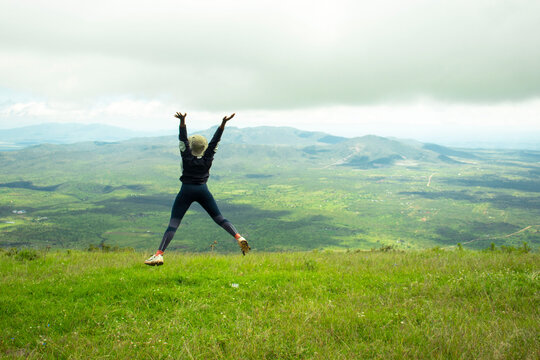 A young black woman frolicking in the grass in the hills after a hike