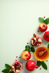 Jewish holiday Rosh Hashanah concept. Top view honey, pomegranate, apples and green leaves on pastel green background.