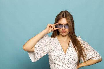 Young woman posing in a dress on a blue background. In blue sunglasses, stylish.