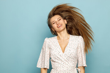 Obraz premium Young woman waving her hair in a dress on a blue background.