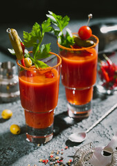 Glasses of bloody mary cocktail with shaker and spoon on dark kitchen board