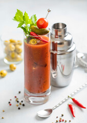 Bloody mary cocktail in highball glass with shaker and spoon on light bar board with olives and red pepper.