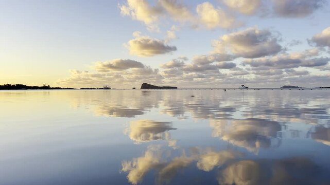 A beautiful and calm sunset view of Gunner's Quoin island from the sea with the sky and clouds reflecting on the glossy ocean water,