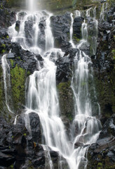 The Poco do Bacalhau waterfall in the Flores island of Azores. Green hills and fields. Sunny weather.
