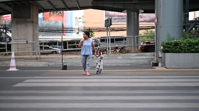 A family is crossing the road on a zebra crossing, the mother is holding the hand of her son to cross the road safely.