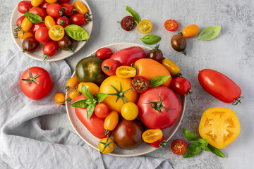 Mixed colorful ripe whole and sliced tomatoes with basil leaves on retro ceramic plate with linen napkin on grey stone table background