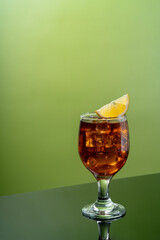 Glass of liquor scotch whiskey with lemon and ice cubes on fresh green background and reflective table top. Space for text