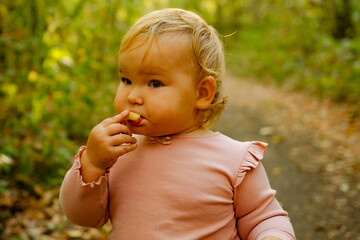 In a vibrant outdoor environment, a joyful baby is savoring food with her fingers, showcasing a curious and playful spirit as she explores her surroundings.