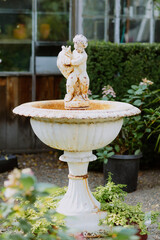 Vintage garden fountain with a weathered cherub statue, surrounded by greenery