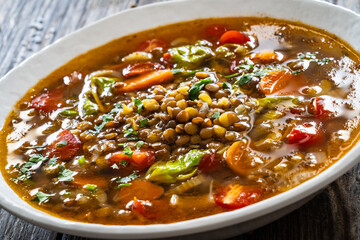Fresh vegetable soup with lentil served in white bowl on wooden table
