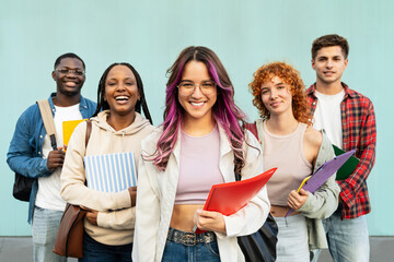 Portrait of hispanic student girl together with college classmate friends. Smiling students standing on university blue wall