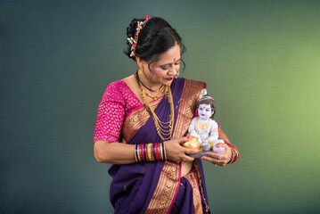 Traditional Indian woman wearing saree posing with God Lord Krishna idol