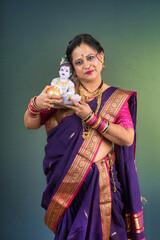Traditional Indian woman wearing saree posing with God Lord Krishna idol