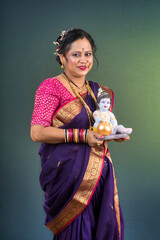 Traditional Indian woman wearing saree posing with God Lord Krishna idol