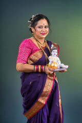 Traditional Indian woman wearing saree posing with God Lord Krishna idol