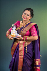 Traditional Indian woman wearing saree posing with God Lord Krishna idol