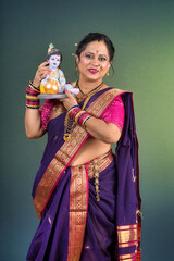 Traditional Indian woman wearing saree posing with God Lord Krishna idol