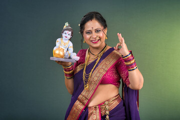 Fototapeta premium Traditional Indian woman wearing saree posing with God Lord Krishna idol