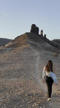 Video de dron con chica guapa en un atardecer con rocas grandes, en un barranco acantilado con el sol poniendose en una bella tarde de las islas canarias en un paraje natural de gran canaria.