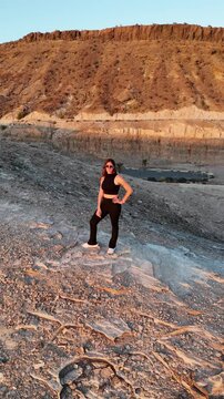 Video de dron con chica guapa en un atardecer con rocas grandes, en un barranco acantilado con el sol poniendose en una bella tarde de las islas canarias en un paraje natural de gran canaria.