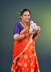 Traditional Indian woman wearing saree posing with God Lord Krishna idol