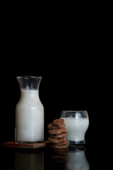 vertical view of a glass of milk and chocolatte cookies with reflective surface table and dark background. Space for text