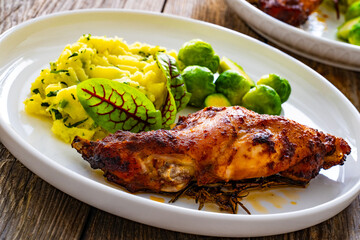 Roast rabbit thigh with mashed potatoes and boiled brussels sprouts served on white plate on wooden background
