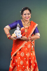 Traditional Indian woman wearing saree posing with God Lord Krishna idol