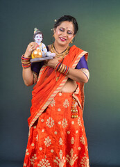 Traditional Indian woman wearing saree posing with God Lord Krishna idol