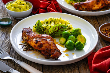Roast rabbit thigh with mashed potatoes and boiled brussels sprouts served on white plate on wooden background
