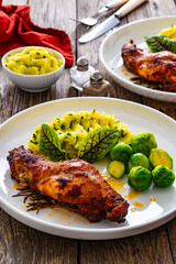 Roast rabbit thigh with mashed potatoes and boiled brussels sprouts served on white plate on wooden background
