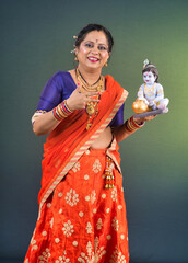 Traditional Indian woman wearing saree posing with God Lord Krishna idol