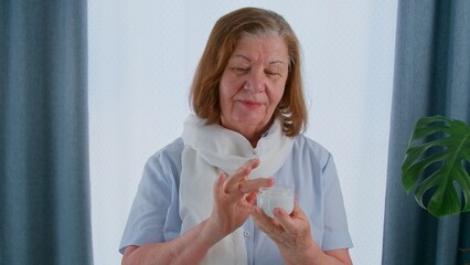 Senior woman applying face moisturizer onto face skin, anti-aging process stopping.