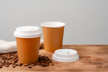 Disposable coffee cups placed on a wooden board with scattered coffee beans and a newspaper