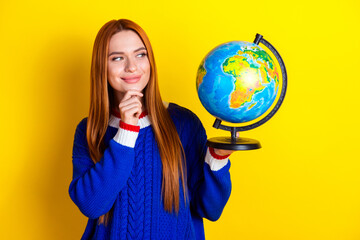 Photo portrait of lovely young lady hold look interested globe dressed stylish blue knitwear garment isolated on yellow color background