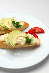 Fresh avocado and cheese spread on toasted bread garnished with cilantro and tomato