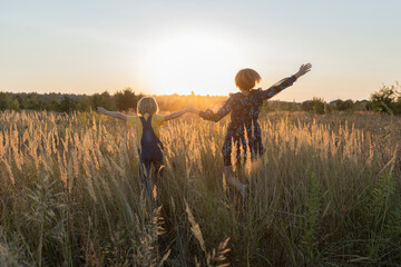 unrecognizable child and woman, mom and son are running across yellow meadow towards sun, spikelets glowing in rays. Happy childhood, walks. Forward to bright future. rear view. Backlight, soft focus