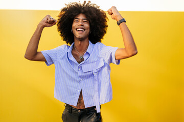 Cheerful gay man holding fists near yellow wall