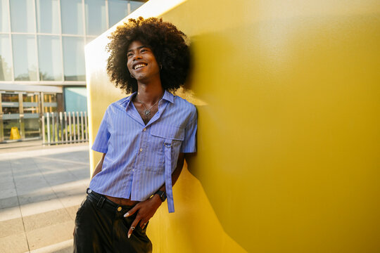 Smiling gay man day dreaming near yellow wall